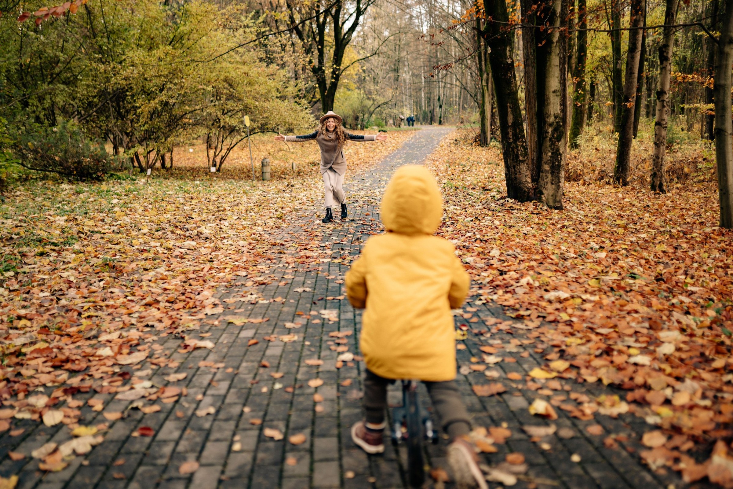 Child on a balance bike riding toward a parent on an autumn path